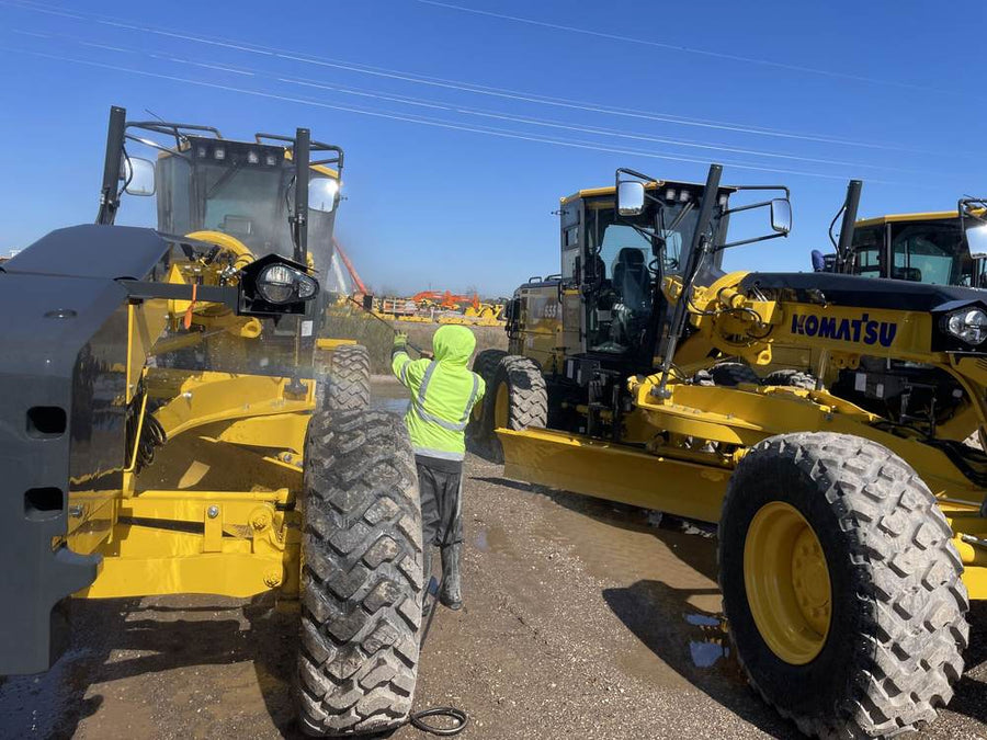Crew cleaning a motor grader on a construction job site