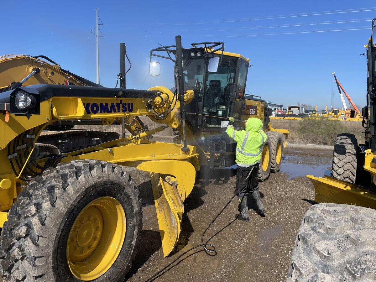 Crew washing a yellow motor grader at a job site
