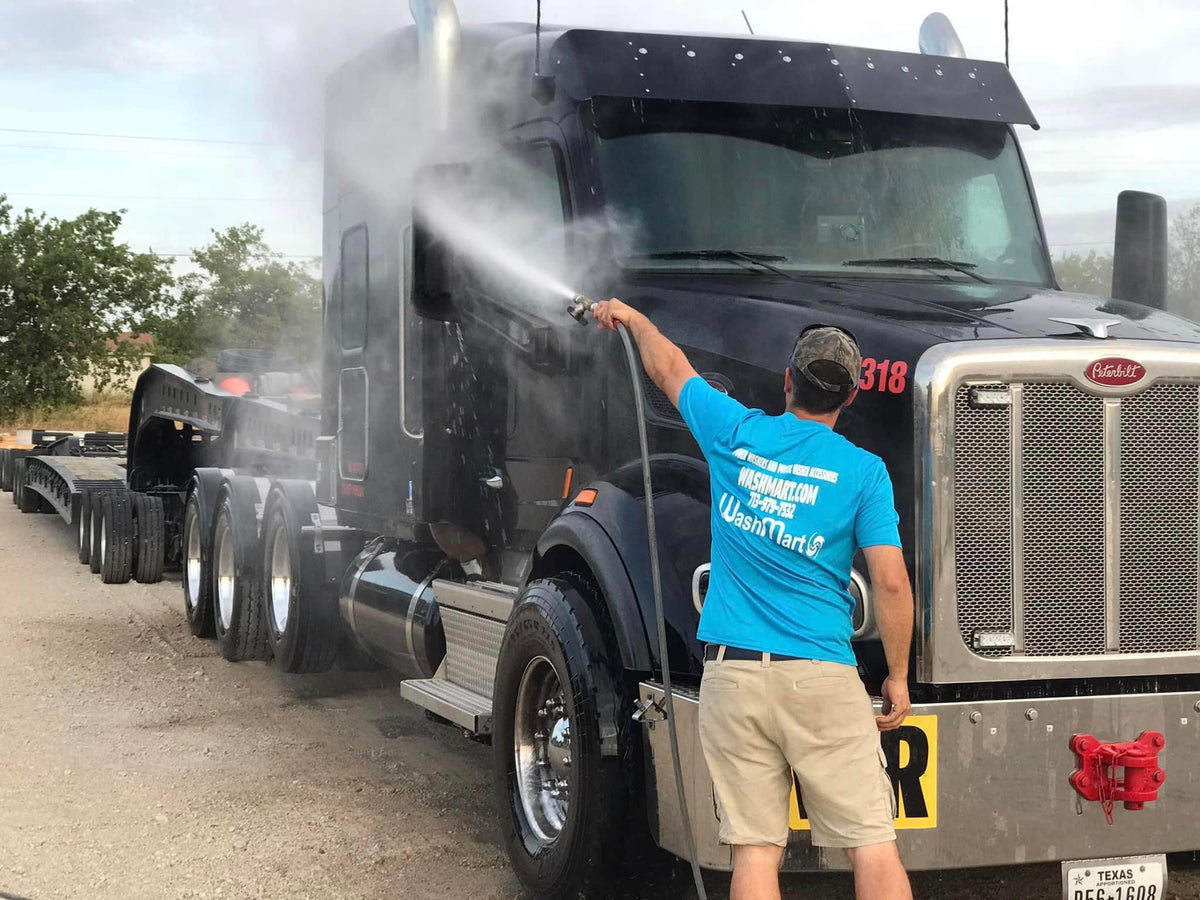 Technician washing a black Peterbilt semi truck
